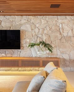 a living room with couches and a flat screen tv mounted on the stone wall