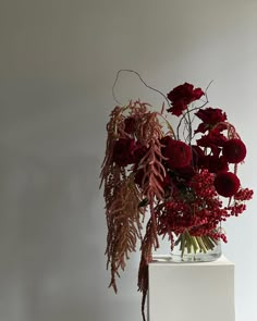 a vase filled with red flowers sitting on top of a white table next to a wall