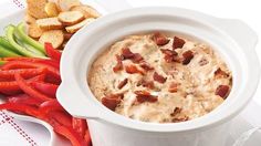 a bowl of dip with bacon on top next to crackers and tomato wedges