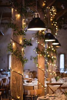 an indoor dining area with wooden pillars and lights hanging from it's ceiling, surrounded by greenery