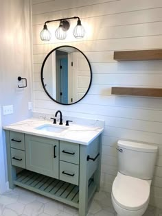 a white toilet sitting next to a bathroom sink under a round mirror on a wall