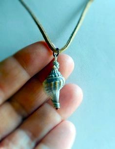 a person is holding a tiny necklace with a shell on it