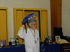 an older woman holding up a blue object in front of her head while standing next to lockers