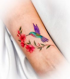 a hummingbird with pink flowers on the left side of the arm and an orange flower in the middle