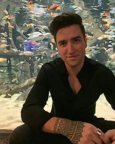 a man sitting in front of a large aquarium filled with lots of different types of fish