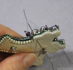 a small toy alligator is being held in someone's hand with beads on it