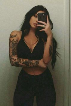 a woman taking a selfie with her cell phone in front of her face and tattoos on her arms