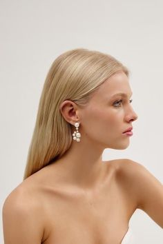 a woman with long blonde hair wearing white earrings and a strapless dress, looking off to the side