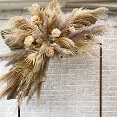 an arrangement of dried flowers and leaves on a stand in front of a white brick wall