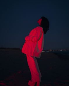 a woman standing on top of a beach next to the ocean under a red light