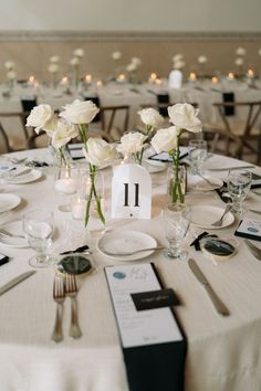 the table is set with white flowers and place settings