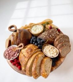 a platter filled with breads, berries and other foods on a white table