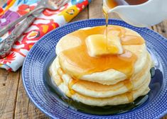 pancakes with syrup being poured onto them on a blue plate