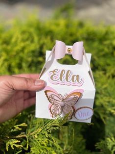 a hand holding a small white box with a pink bow on it's side