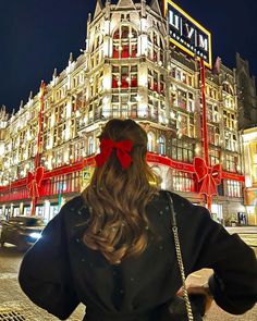 a woman standing in front of a building with a red bow on her head and long hair