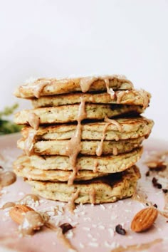 a stack of pancakes with almonds and drizzled on top, sitting on a pink plate