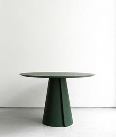 a round green table sitting on top of a white floor in front of a wall