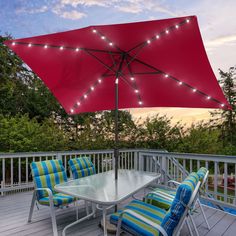 an umbrella and chairs on a deck with trees in the background