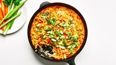 a skillet filled with food next to a plate of carrots and celery