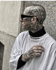 a man with tattoos and piercings on his face standing in front of a building