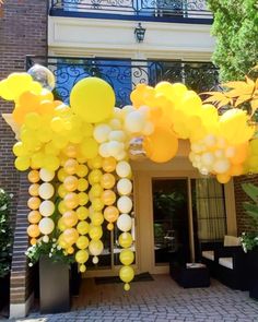 yellow and white balloons are hanging from the outside of a building in front of an entrance