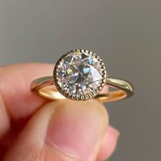 a close up of a person's hand holding a ring with a diamond in it