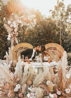 a bride and groom kissing at an outdoor table surrounded by pamodia