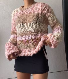 a woman wearing a pink sweater and black skirt standing in front of a white wall