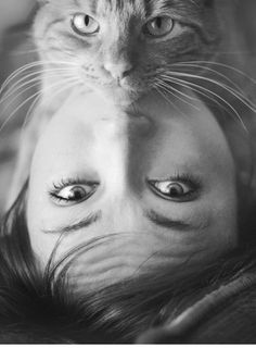 black and white photograph of a woman with a cat on her head looking at the camera