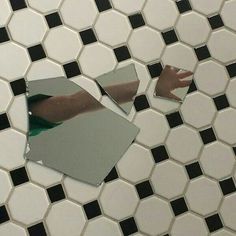 a person's reflection in a mirror on a tiled floor with black and white tiles