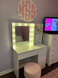 a white vanity with lights on it and a television in the corner next to it