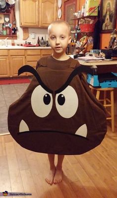 a young boy is standing in the kitchen holding a towel with an angry face on it