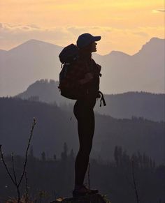 a person standing on top of a mountain with a backpack in their hands and the sun setting behind them