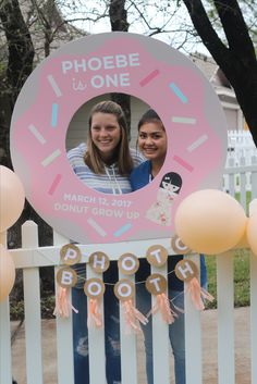 two girls standing in front of a sign with doughnuts on it that says, phoebe is one