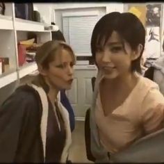 two women standing next to each other in a room with bookshelves and shelves