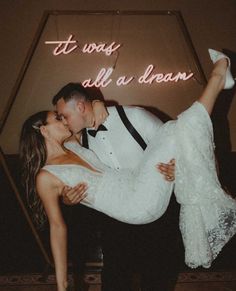 a bride and groom kissing in front of a neon sign that says it was all a dream