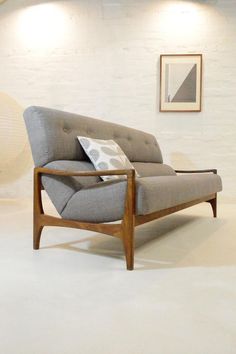 a gray couch sitting on top of a white floor next to a framed painting and wooden frame