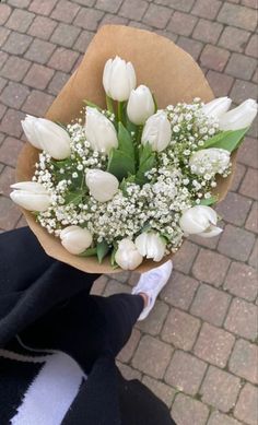 a bouquet of white tulips and baby's breath is held by someone