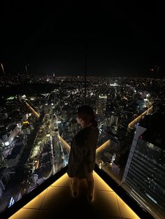 a woman standing on top of a tall building at night looking out over the city