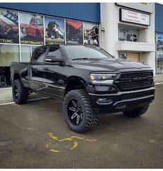 a black ram truck parked in front of a building with large tires on it's tires