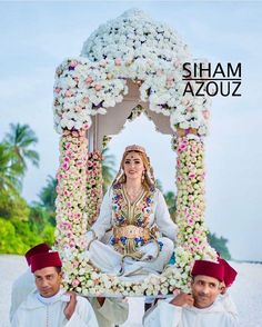 a woman sitting on top of a man in front of a flower covered structure with two men standing next to her