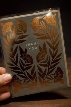 a person holding up a card that says thank you with gold foil flowers on it