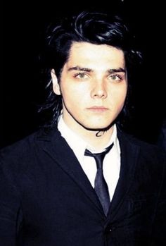 a man with long black hair wearing a suit and tie, looking at the camera