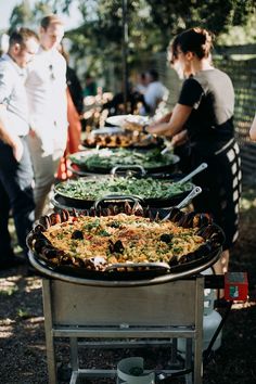 a buffet table filled with lots of food and people standing around the tables looking at it