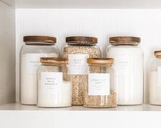 jars with labels are lined up on a shelf in a kitchen, one is filled with grains and the other contains oatmeal