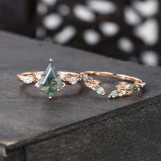 two rings with green and white stones sitting on top of a wooden table next to each other