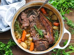 pot roast with carrots, potatoes and parsley in a white dutch oven on a wooden table