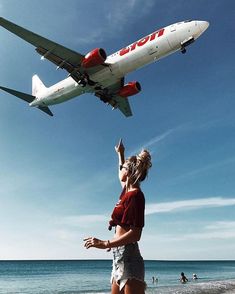 two women standing on the beach looking at an airplane flying over their heads in the air