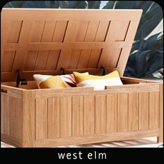 an open wooden chest sitting on top of a white table next to pillows and plants