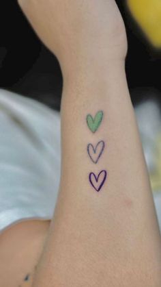 three hearts tattoo on the left side of the ankle, with green and blue ink